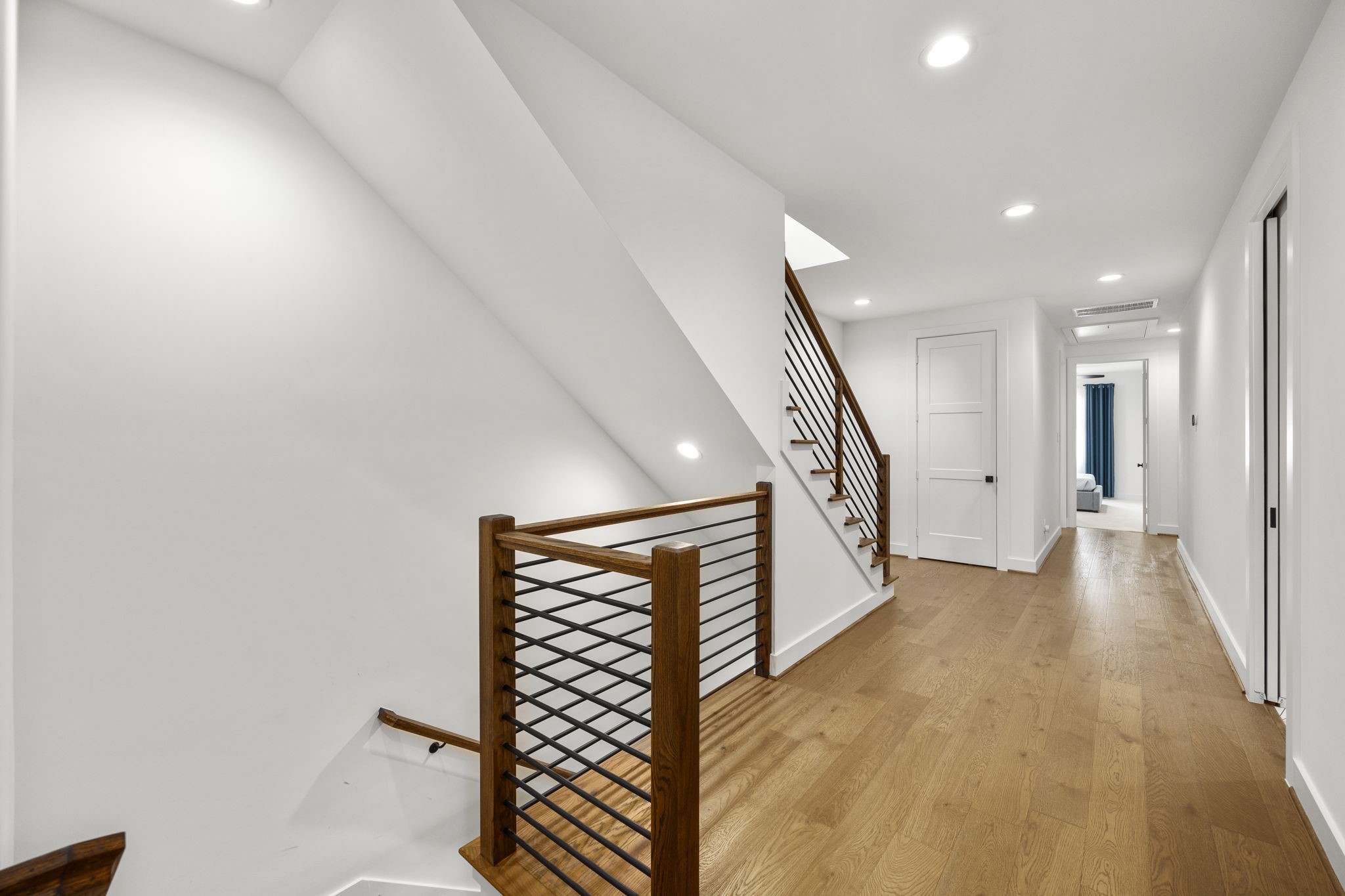 2411 Hazard Street Houston, TX 77019 - Photo 33 of 46 This view of the second-floor landing showcases the elegant staircase with modern wood and metal railings. The hallway features warm wood flooring and leads to additional rooms, offering an open and airy space enhanced by clean lines and recessed lighting. The layout seamlessly connects the upper floor with the rest of the home, creating a natural flow.