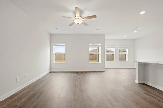 an empty room with wooden floor chandelier fan and windows
