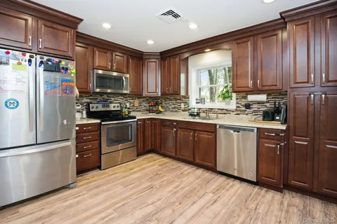 a kitchen with stainless steel appliances granite countertop wooden cabinets a refrigerator a sink a stove a microwave and wooden floors