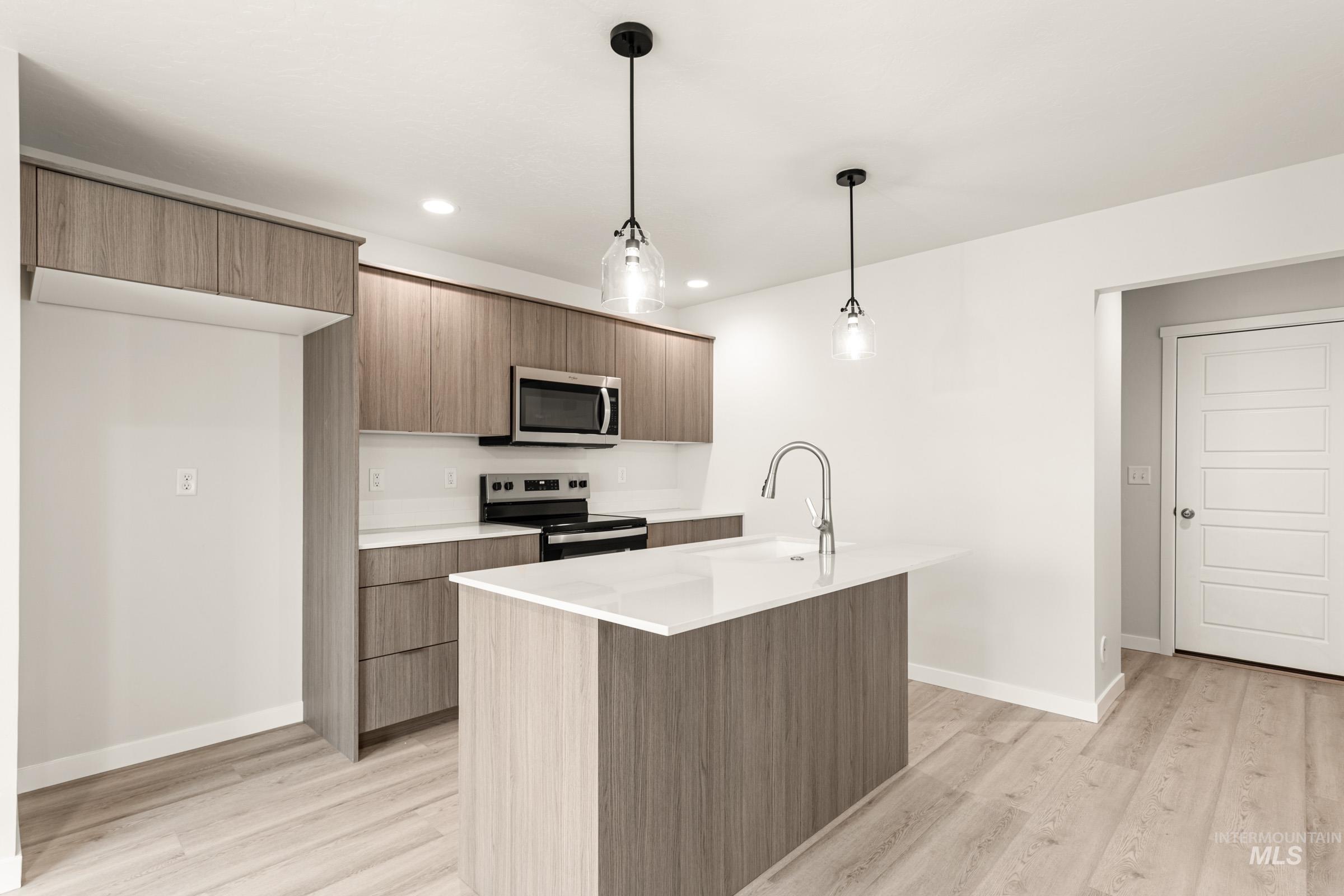 10832 Rutland Street Caldwell, ID 83605 - Photo 3 of 20 Kitchen with stainless steel appliances, hanging light fixtures, a kitchen island with sink, light wood-type flooring, and modern cabinets