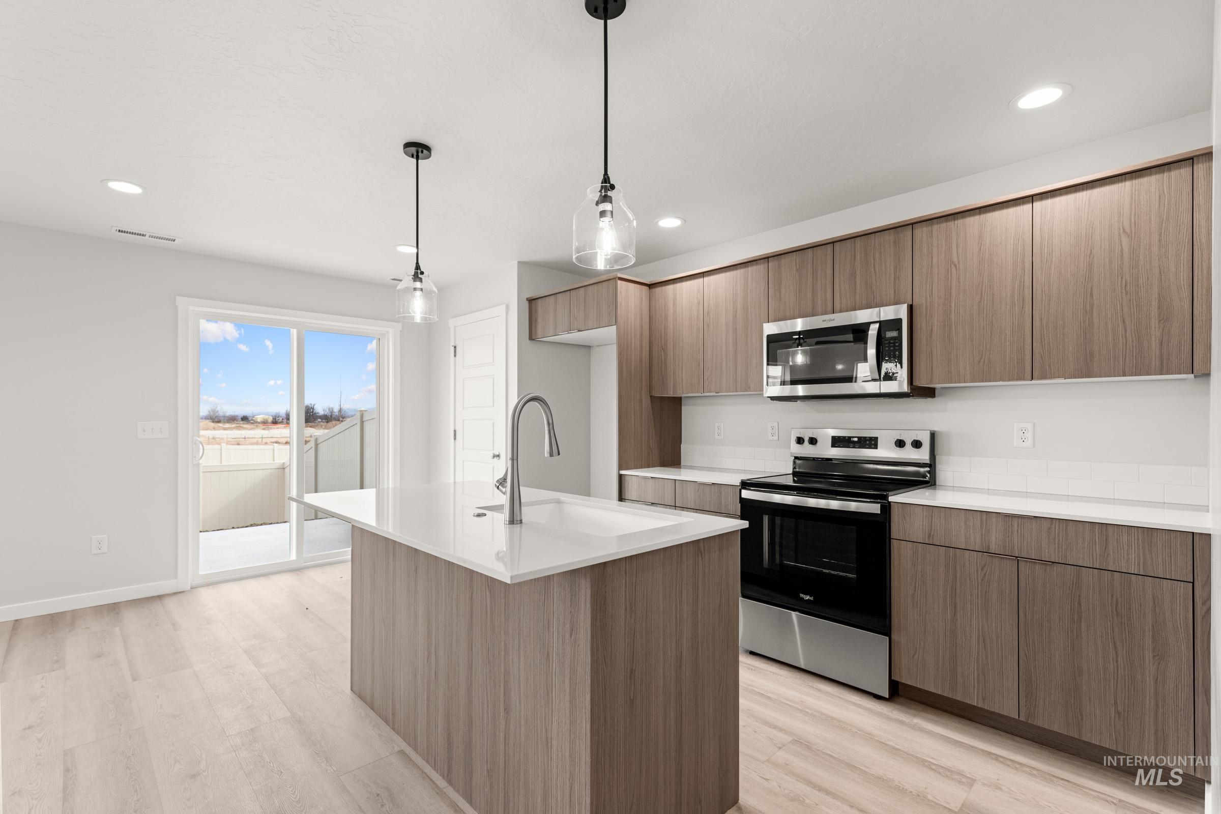 10832 Rutland Street Caldwell, ID 83605 - Photo 6 of 20 Kitchen with stainless steel appliances, decorative light fixtures, a kitchen island with sink, light wood-style flooring, and modern cabinets