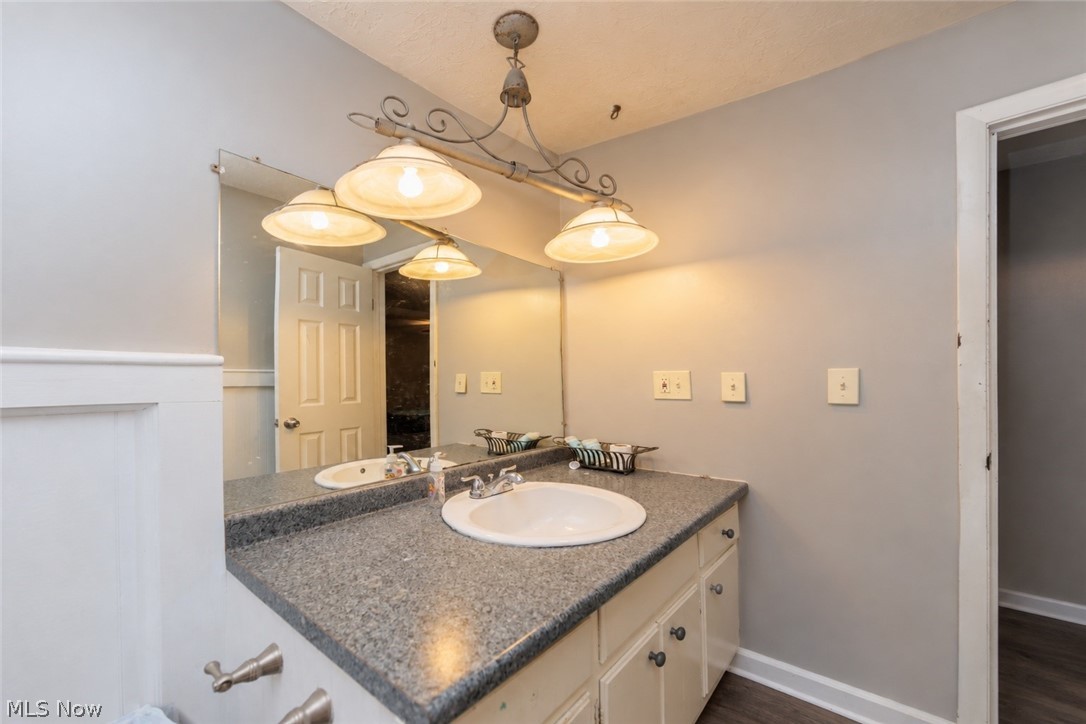6065 Avon Belden Road North Ridgeville, OH 44039 - Photo 17 of 25 Dual vanity with integrated sinks, speckled countertop, cream cabinetry, and wall-mounted lighting fixture