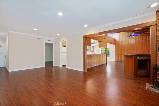 a view of an empty room with wooden floor and a kitchen