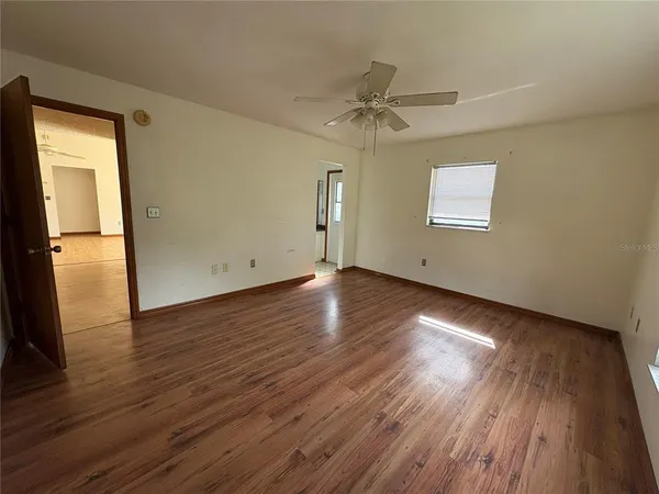 a view of an empty room with wooden floor and a ceiling fan