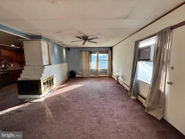 a view of a livingroom with a fireplace a ceiling fan and windows