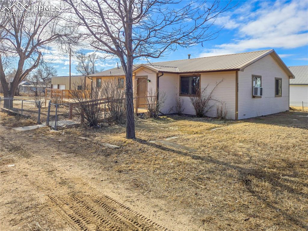 View of side of property with cooling unit, a yard, metal roof, and fence