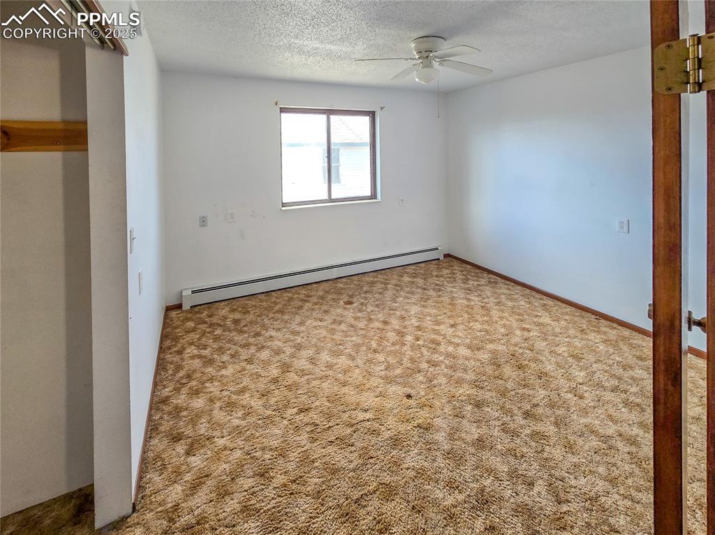 722 6th Street Hugo, CO 80821 - Photo 20 of 35 Unfurnished bedroom with a textured ceiling, a baseboard heating unit, ceiling fan, and carpet