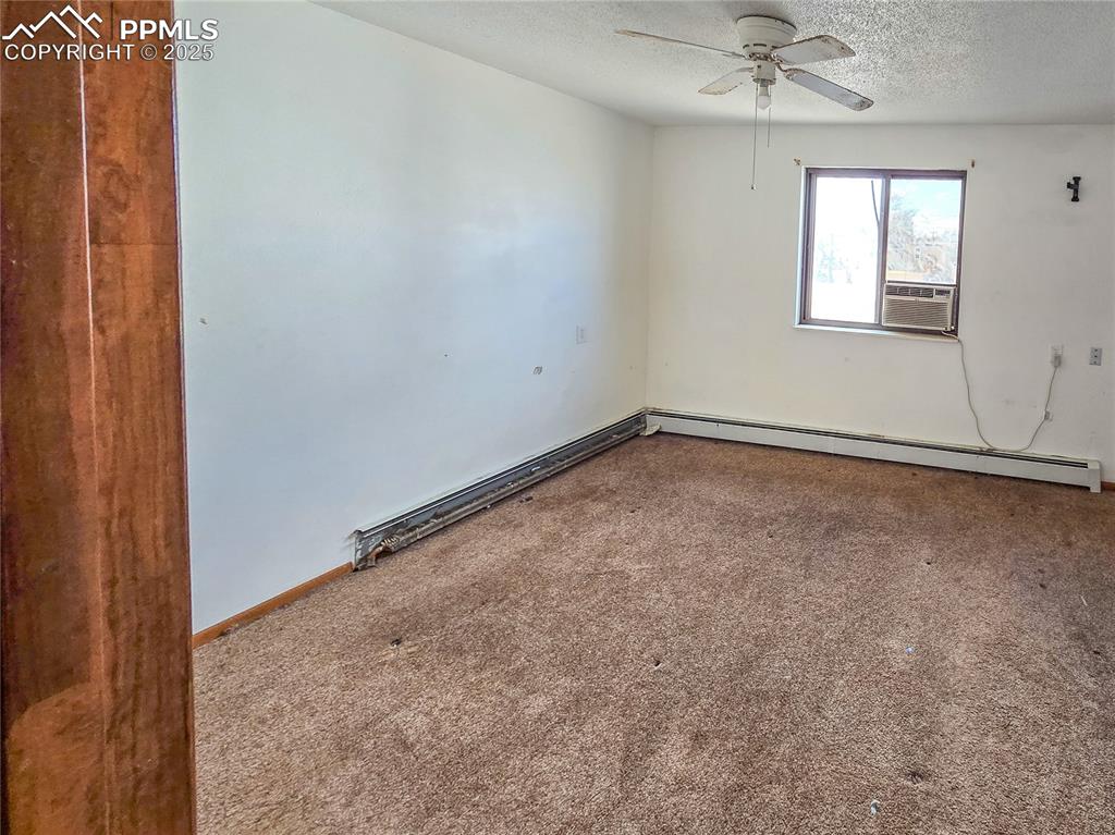 722 6th Street Hugo, CO 80821 - Photo 24 of 35 Carpeted spare room featuring a baseboard radiator, a ceiling fan, cooling unit, and a textured ceiling