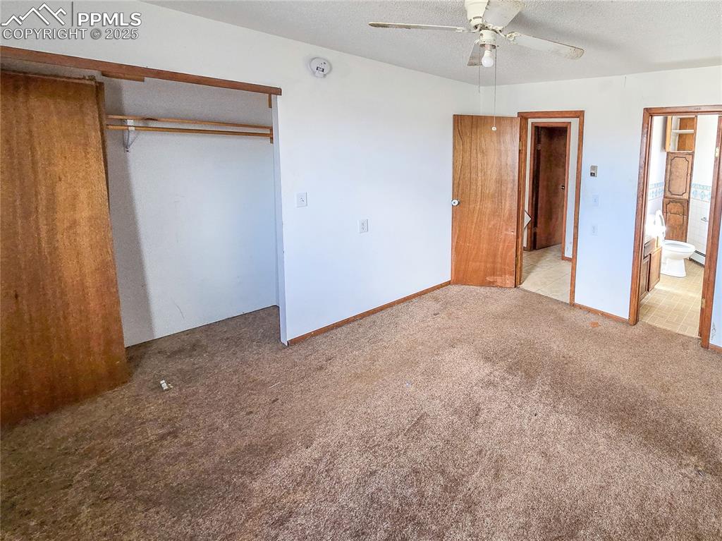 722 6th Street Hugo, CO 80821 - Photo 25 of 35 Unfurnished bedroom with connected bathroom, a textured ceiling, a closet, a ceiling fan, and carpet floors