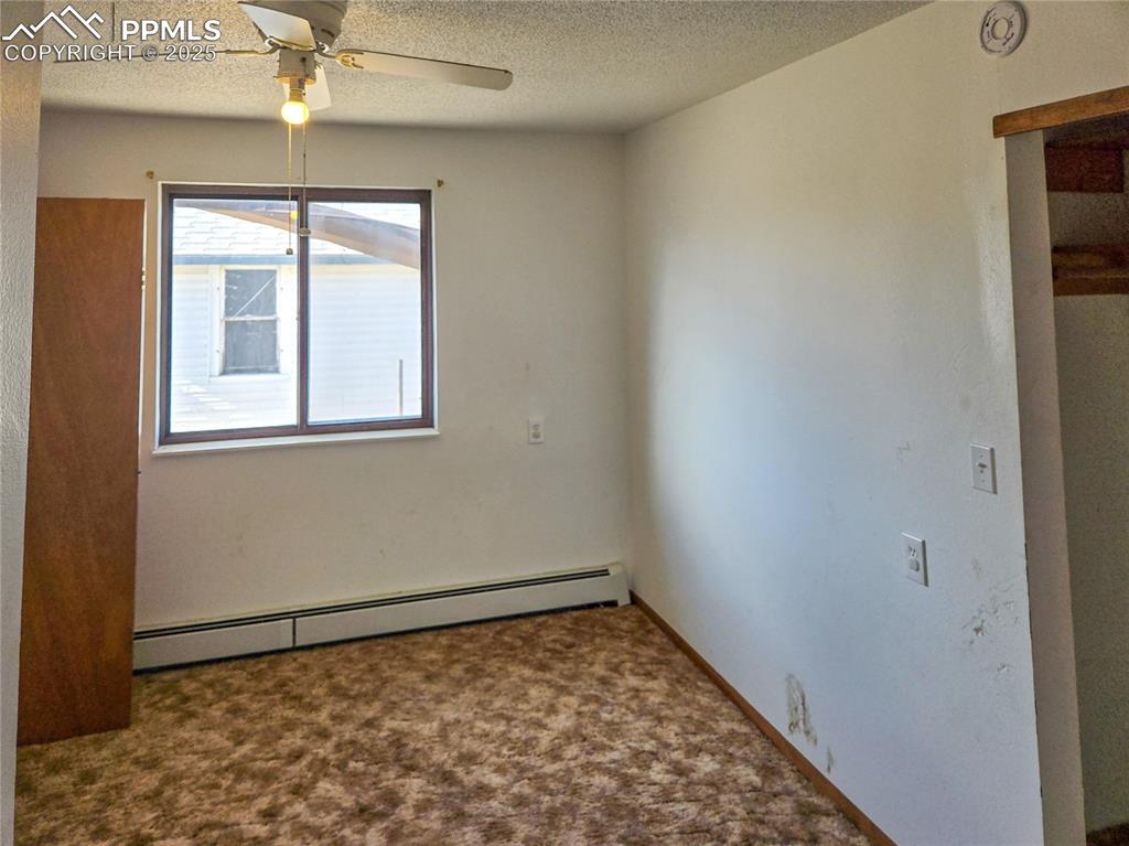 722 6th Street Hugo, CO 80821 - Photo 33 of 35 Carpeted empty room featuring baseboard heating, a textured ceiling, and a ceiling fan