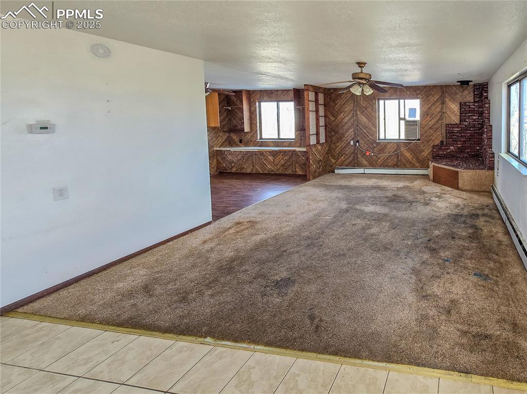 722 6th Street Hugo, CO 80821 - Photo 8 of 35 Unfurnished living room featuring baseboards, a baseboard radiator, ceiling fan, carpet, and wooden walls