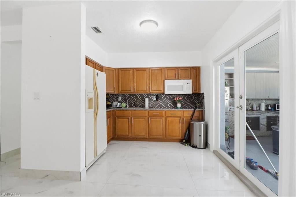 6800 Northwest 28th Avenue Miami, FL 33147 - Photo 13 of 40 Kitchen with brown cabinetry, white appliances, and decorative backsplash