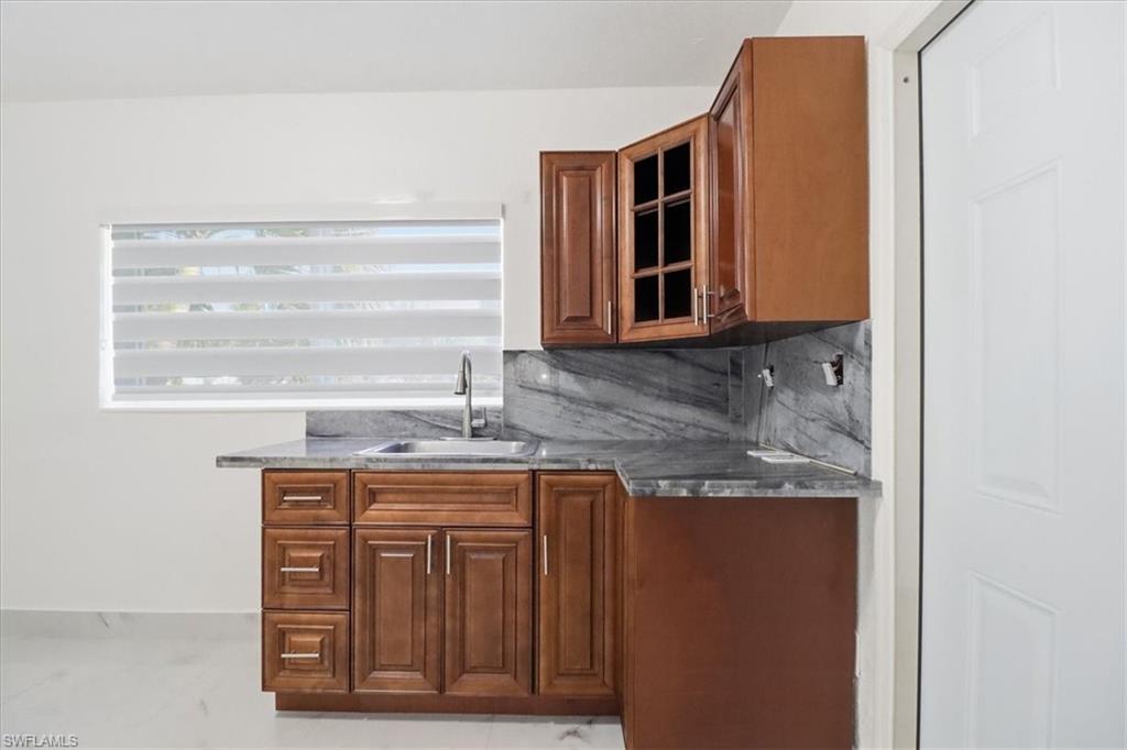 6800 Northwest 28th Avenue Miami, FL 33147 - Photo 18 of 40 Bar area featuring brown cabinets, decorative backsplash, glass insert cabinets, and dark stone countertops