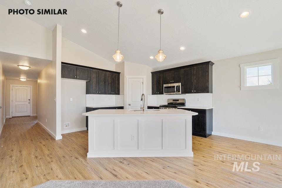 1708 Rapid Road Emmett, ID 83617 - Photo 10 of 33 Open-concept kitchen featuring an island with white paneling, dark wood cabinetry, stainless steel appliances, a subway tile backsplash, and light wood-finish flooring