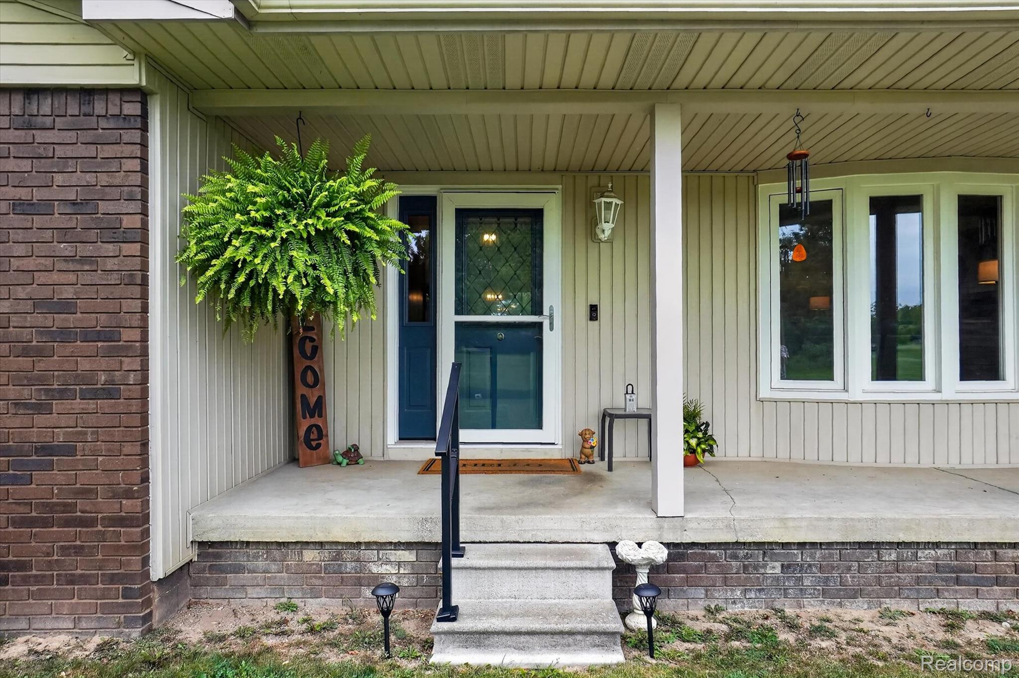 6895 Stow Road Fowlerville, MI 48836 - Photo 45 of 45 Brick and siding exterior with a covered concrete porch, detailed front door, bay windows, and exterior lighting