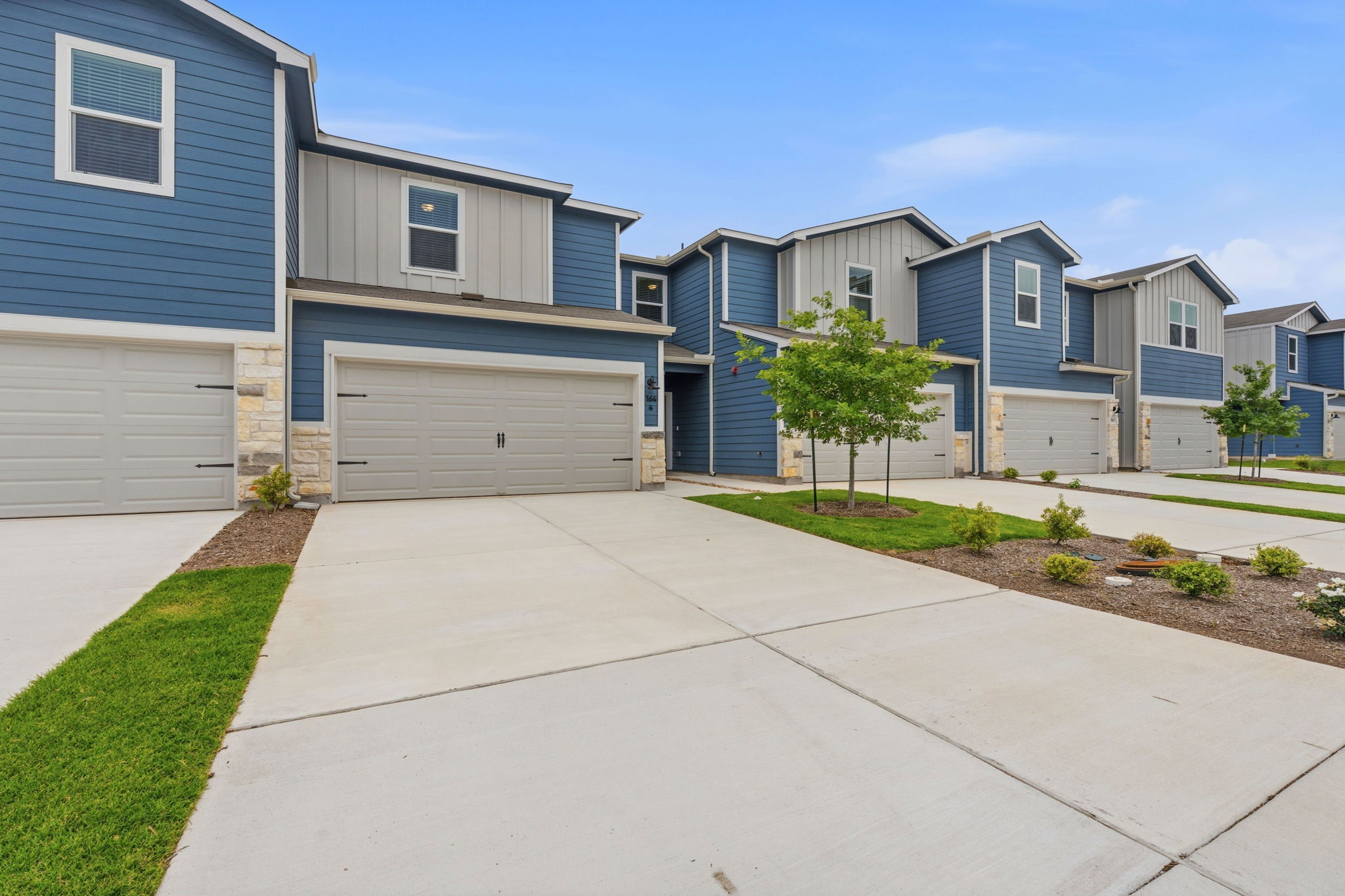 164 Cinnabar Lane, Unit 4 Kyle, TX 78640 - Photo 1 of 23 Modern townhome exterior featuring blue siding, vertical gray siding accents, and stone veneer detailing
