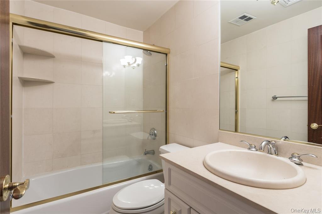 171 Great Neck Road, Unit 1N Great Neck, NY 11021 - Photo 11 of 15 Full bath with vanity, shower / bath combination with glass door, and tile walls