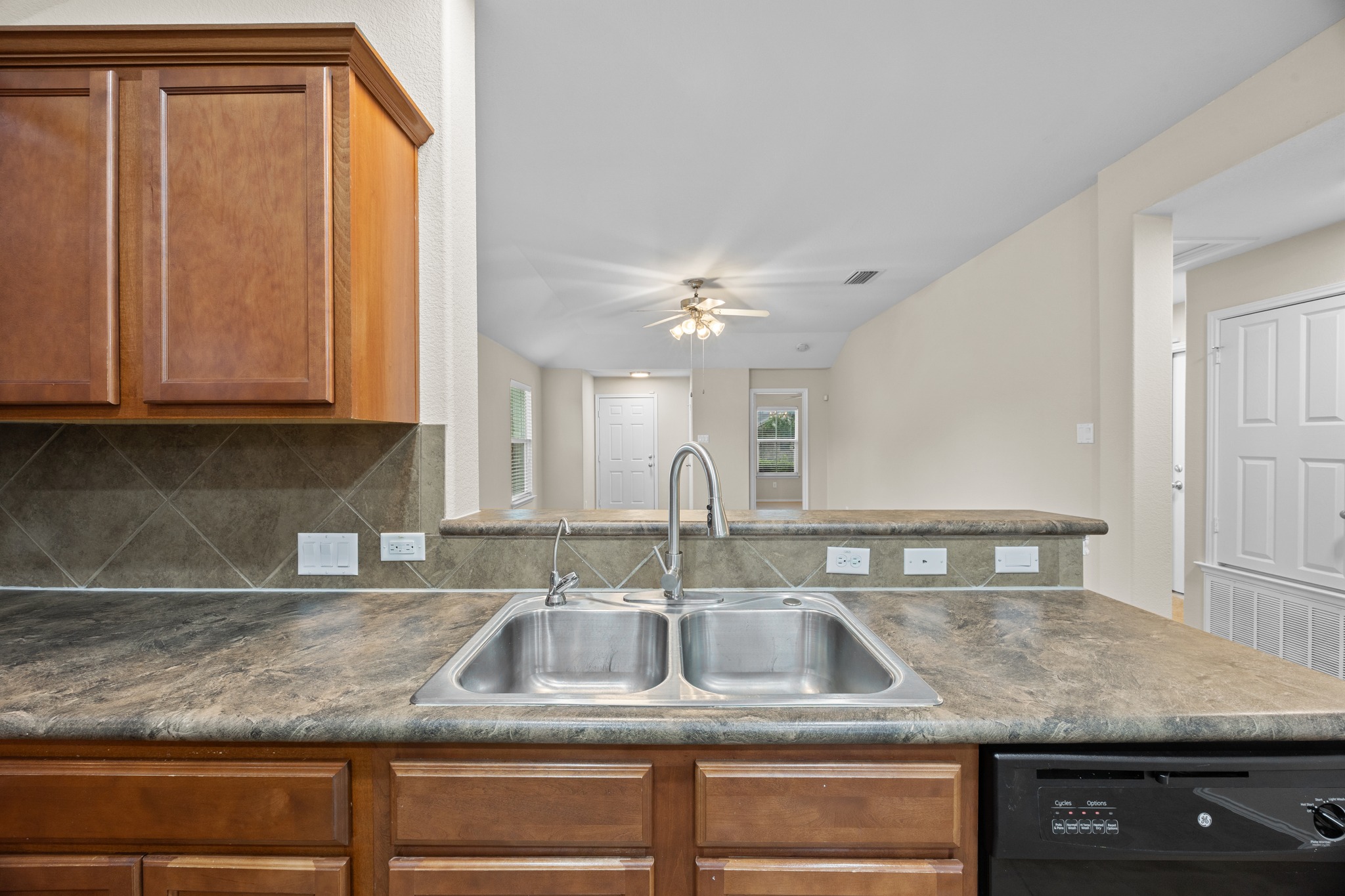 418 Nottingham Loop Kyle, TX 78640 - Photo 11 of 28 Kitchen featuring a double-basin stainless steel sink, a high-arc faucet, wood cabinetry, a tiled backsplash, and a breakfast bar with a stone-finish countertop