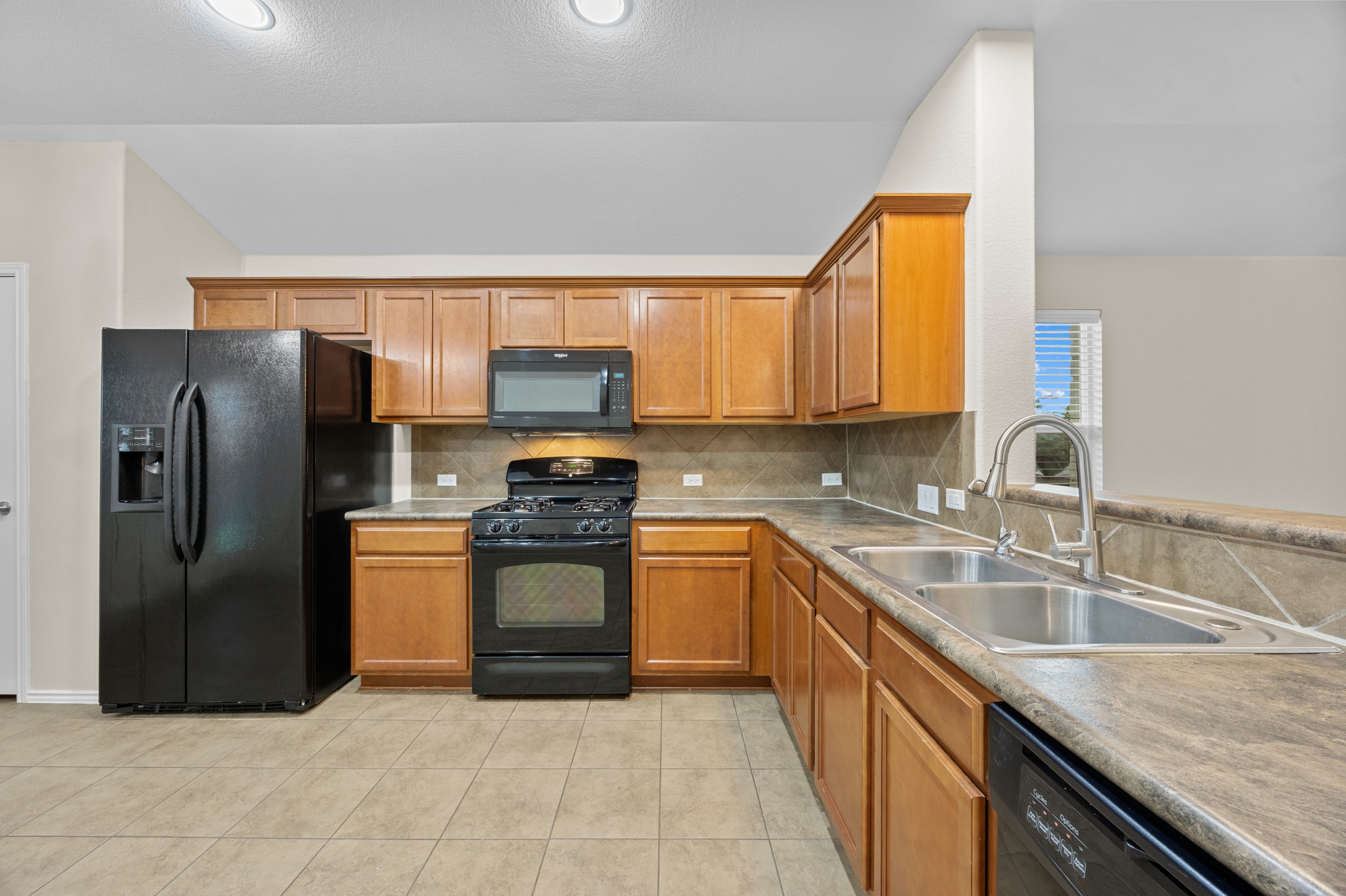 418 Nottingham Loop Kyle, TX 78640 - Photo 12 of 28 Kitchen featuring wood cabinetry, black appliances, a double basin sink with a gooseneck faucet, tile flooring, and a tile backsplash