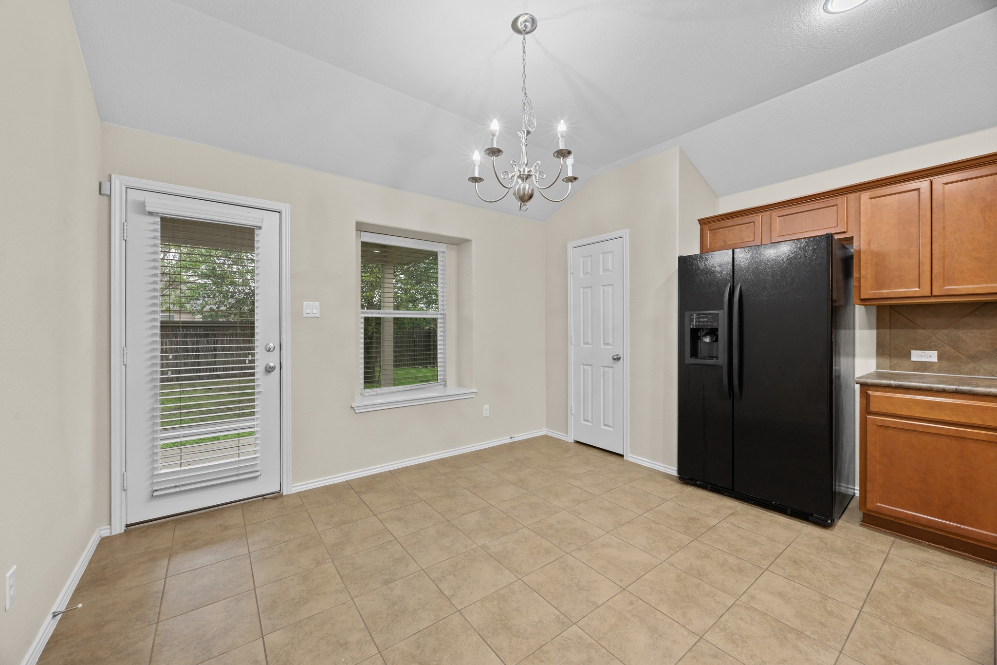 418 Nottingham Loop Kyle, TX 78640 - Photo 13 of 28 Kitchen dining area featuring neutral tile flooring, a contemporary chandelier, and a rear exterior door with integrated blinds