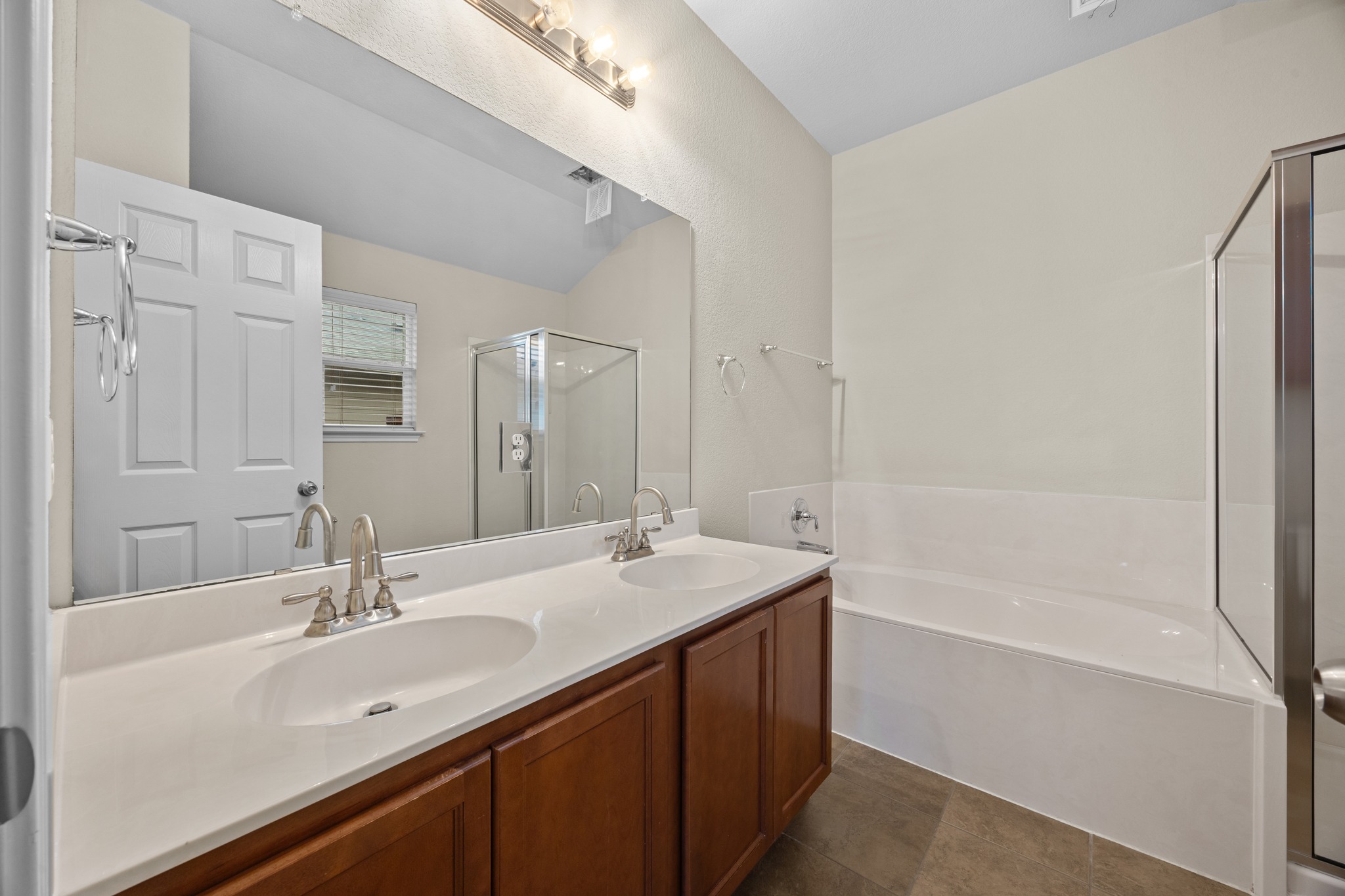418 Nottingham Loop Kyle, TX 78640 - Photo 20 of 28 Dual vanity with white countertops and undermount sinks, bronze-toned cabinetry, a built-in bathtub, and a separate glass-enclosed shower