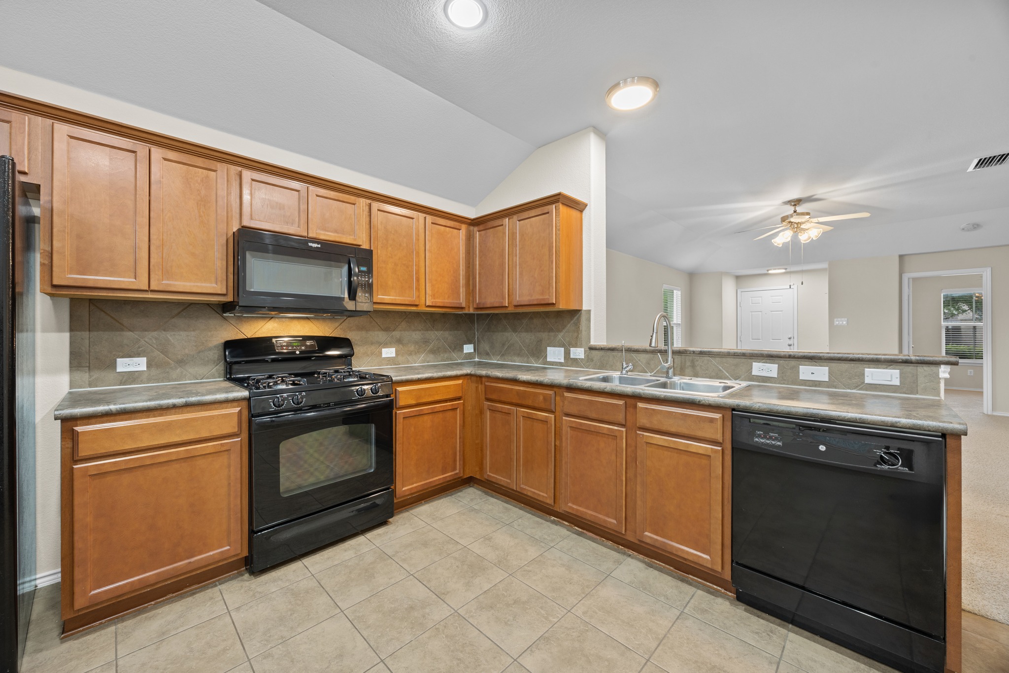 418 Nottingham Loop Kyle, TX 78640 - Photo 10 of 28 Kitchen featuring wood-finish cabinetry, a black appliance suite, and a tile backsplash