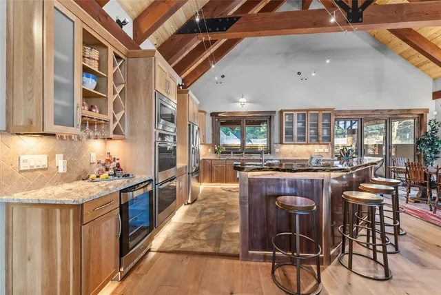 a kitchen with stainless steel appliances granite countertop a stove top oven a sink a dining table and chairs with wooden floor