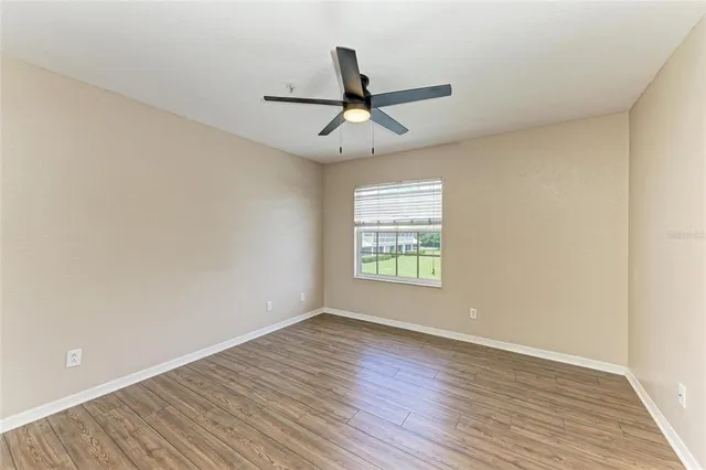 an empty room with wooden floor fan and windows