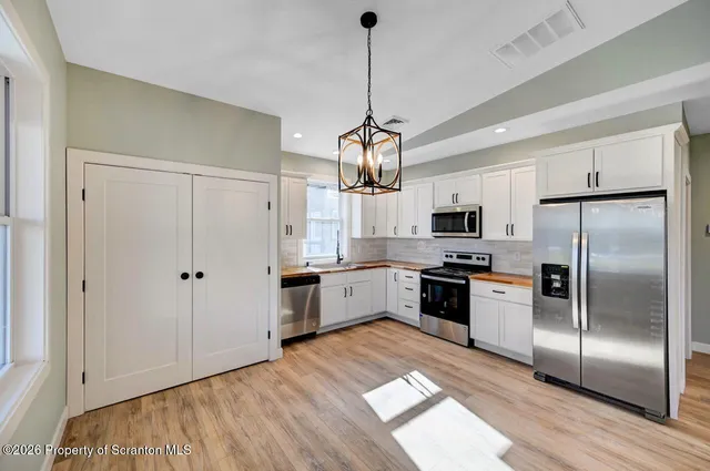 a kitchen with granite countertop a refrigerator oven a sink dishwasher and white cabinets with wooden floor