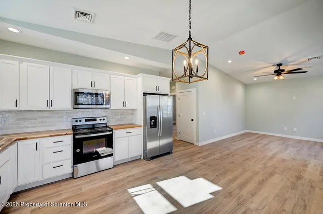 a kitchen with stainless steel appliances granite countertop a refrigerator a stove and white cabinets with wooden floor