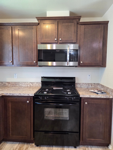 1275 Thrush Road Salt Lake City, UT 84123 - Photo 6 of 20 Kitchen featuring a black gas range, a stainless steel over-the-range microwave, and dark wood cabinetry with light-toned countertops