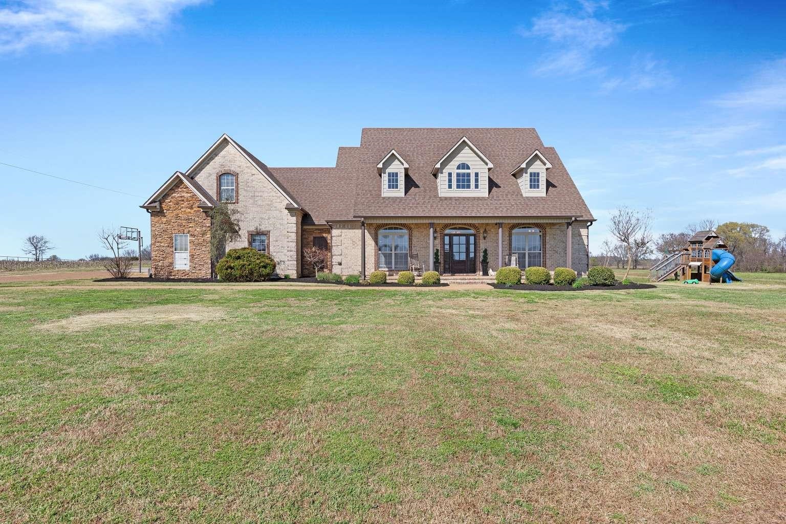 View of front of house with covered porch, a front yard, stone siding, brick siding, and a playground