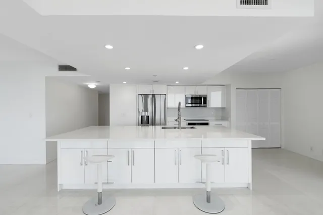 a large white kitchen with kitchen island a sink stainless steel appliances and cabinets