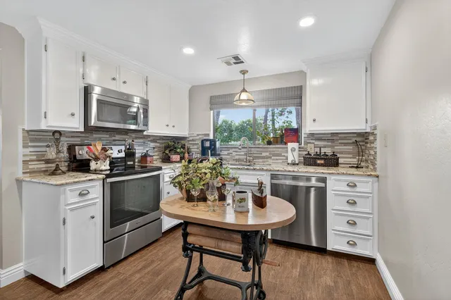 a kitchen with stainless steel appliances kitchen island granite countertop a refrigerator a stove a sink dishwasher and white cabinets with wooden floor