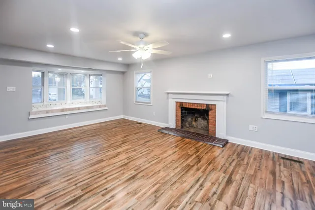 a view of an empty room with wooden floor fireplace and a window