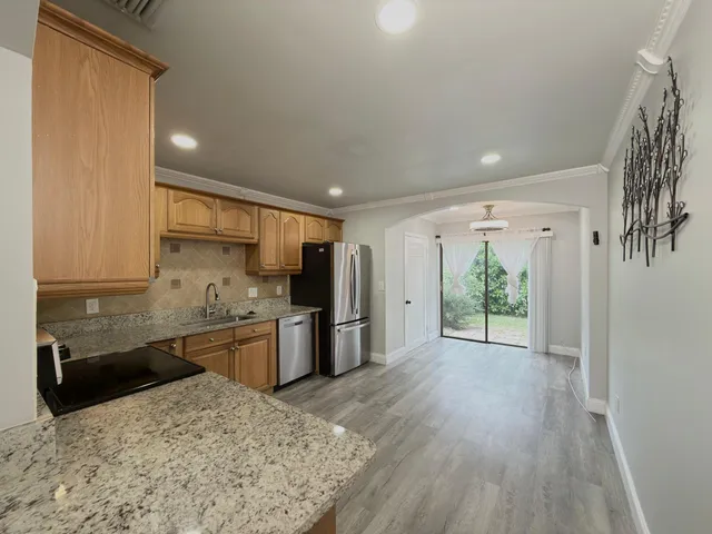 a large kitchen with stainless steel appliances granite countertop a refrigerator a stove a sink dishwasher and wooden cabinets with wooden floor