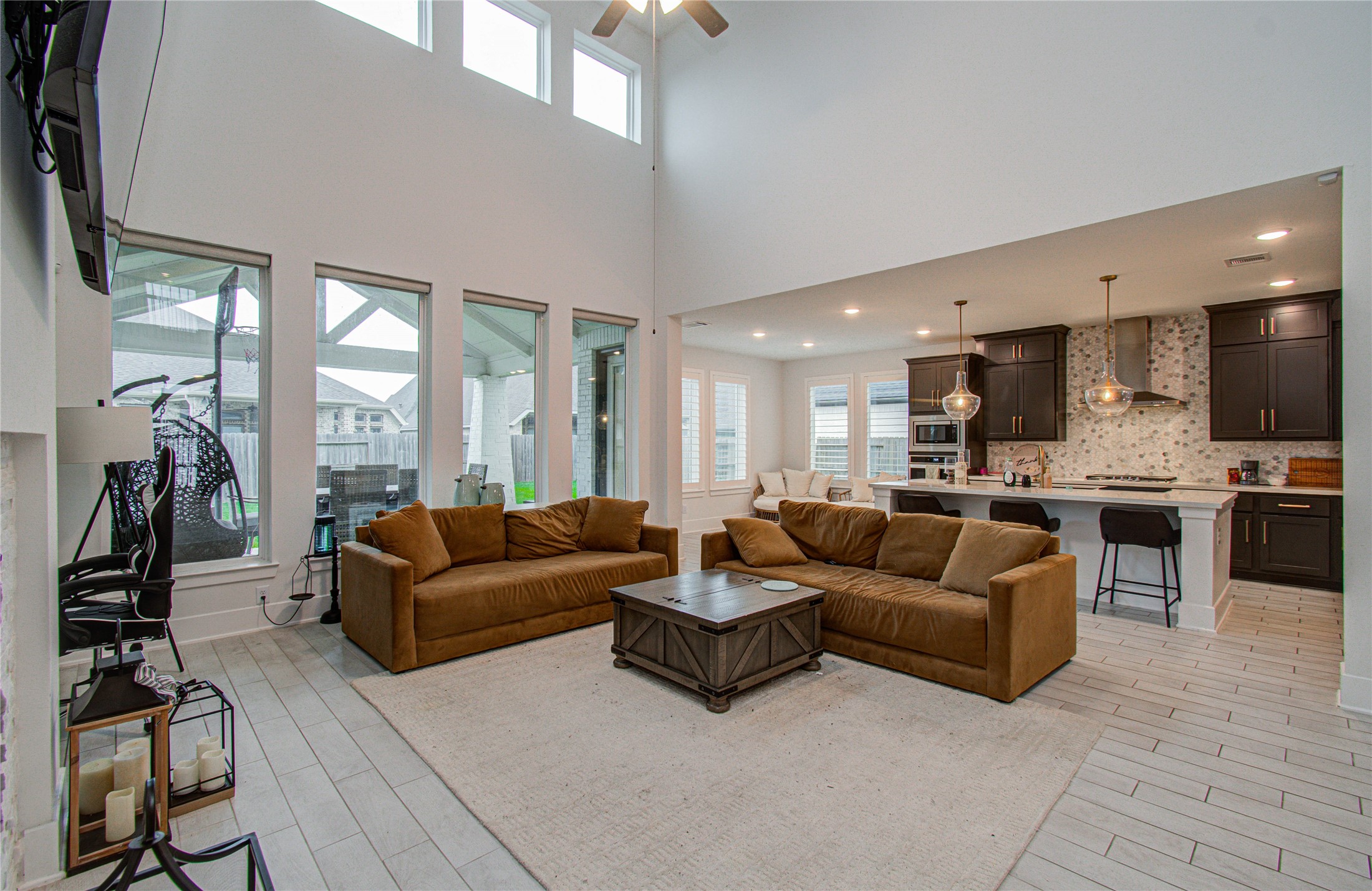 4211 Limestone Terrace Manvel, TX 77578 - Photo 13 of 33 This spacious open-concept living area features high ceilings and ample natural light, with large windows overlooking the backyard. It seamlessly connects to a modern kitchen with dark cabinetry, stainless steel appliances, and stylish pendant lighting over a breakfast bar. Cozy seating and a neutral color palette create a welcoming atmosphere.