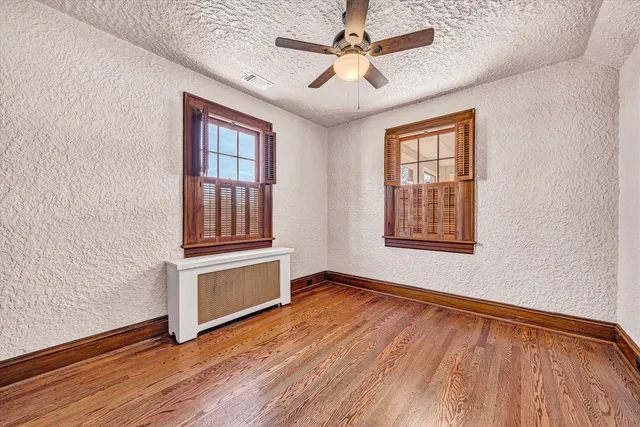 an empty room with wooden floor chandelier fan and windows
