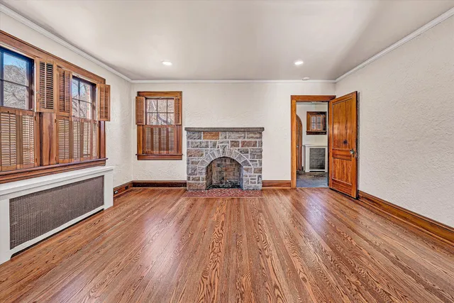 a view of an empty room with wooden floor fireplace and a window