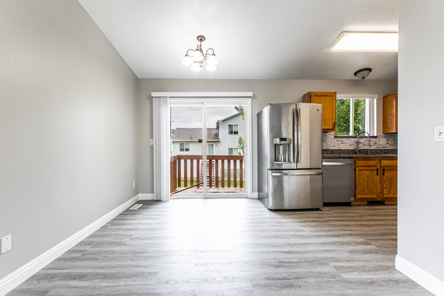 4239 West 5325th Street South Roy, UT 84067 - Photo 6 of 26 Wood-finish flooring throughout, with a stainless steel refrigerator, and a sliding glass door opening to an outdoor deck