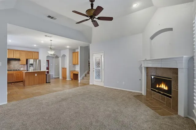 a view of a livingroom with a fireplace a ceiling fan and a kitchen view