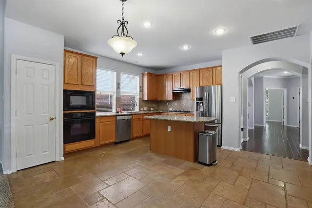 a kitchen with stainless steel appliances granite countertop a refrigerator a sink dishwasher a stove and white cabinets with wooden floor