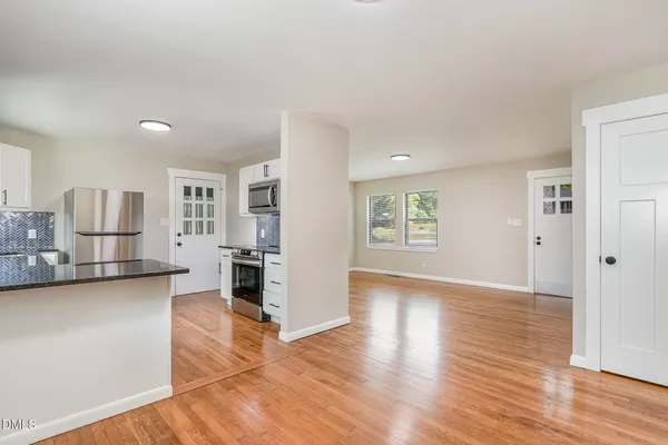a view of empty room with wooden floor and kitchen
