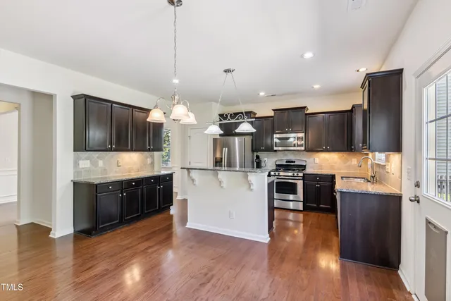 a kitchen with stainless steel appliances kitchen island granite countertop a refrigerator a stove a sink dishwasher and a oven with wooden floor
