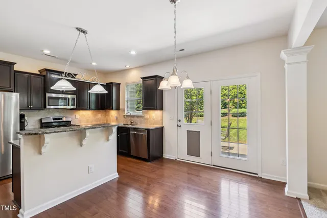 a kitchen with stainless steel appliances kitchen island granite countertop a stove a sink a refrigerator a center island and wooden floor