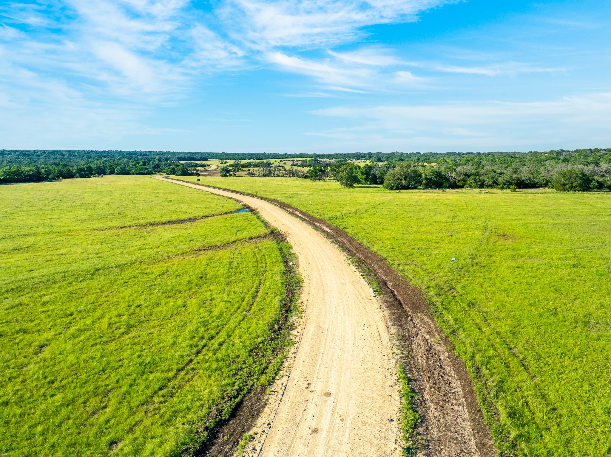 32 Feild Ranch Road Burnet, TX 78611 - Photo 7 of 40 Vast green meadows unfold under an open sky, bisected by a winding dirt road.