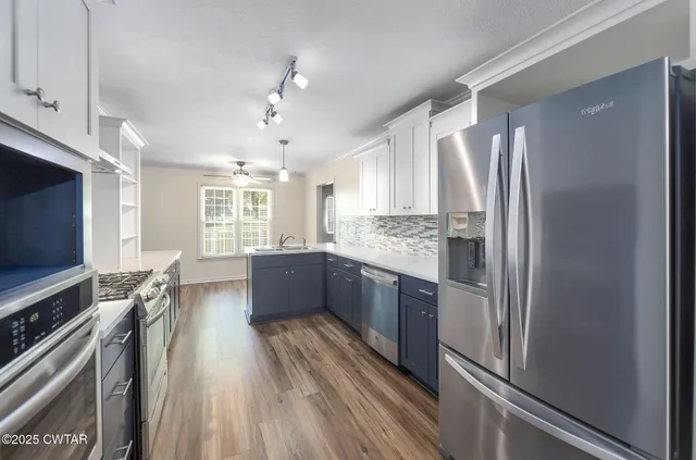 a kitchen with stainless steel appliances granite countertop a refrigerator a sink dishwasher a stove and white countertops with wooden floor