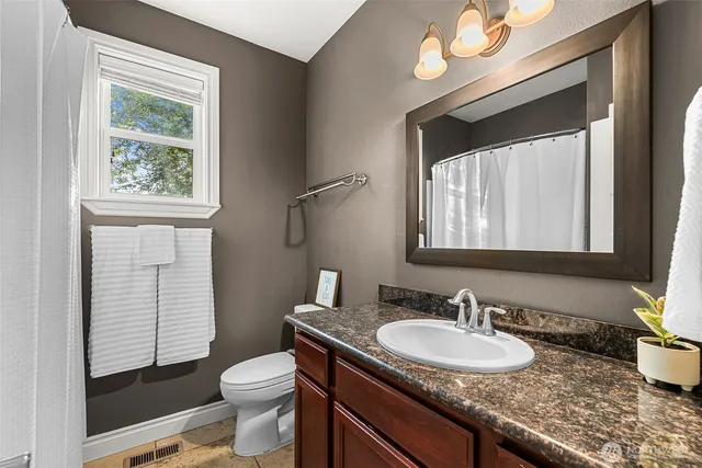 a bathroom with a granite countertop sink vanity mirror and toilet