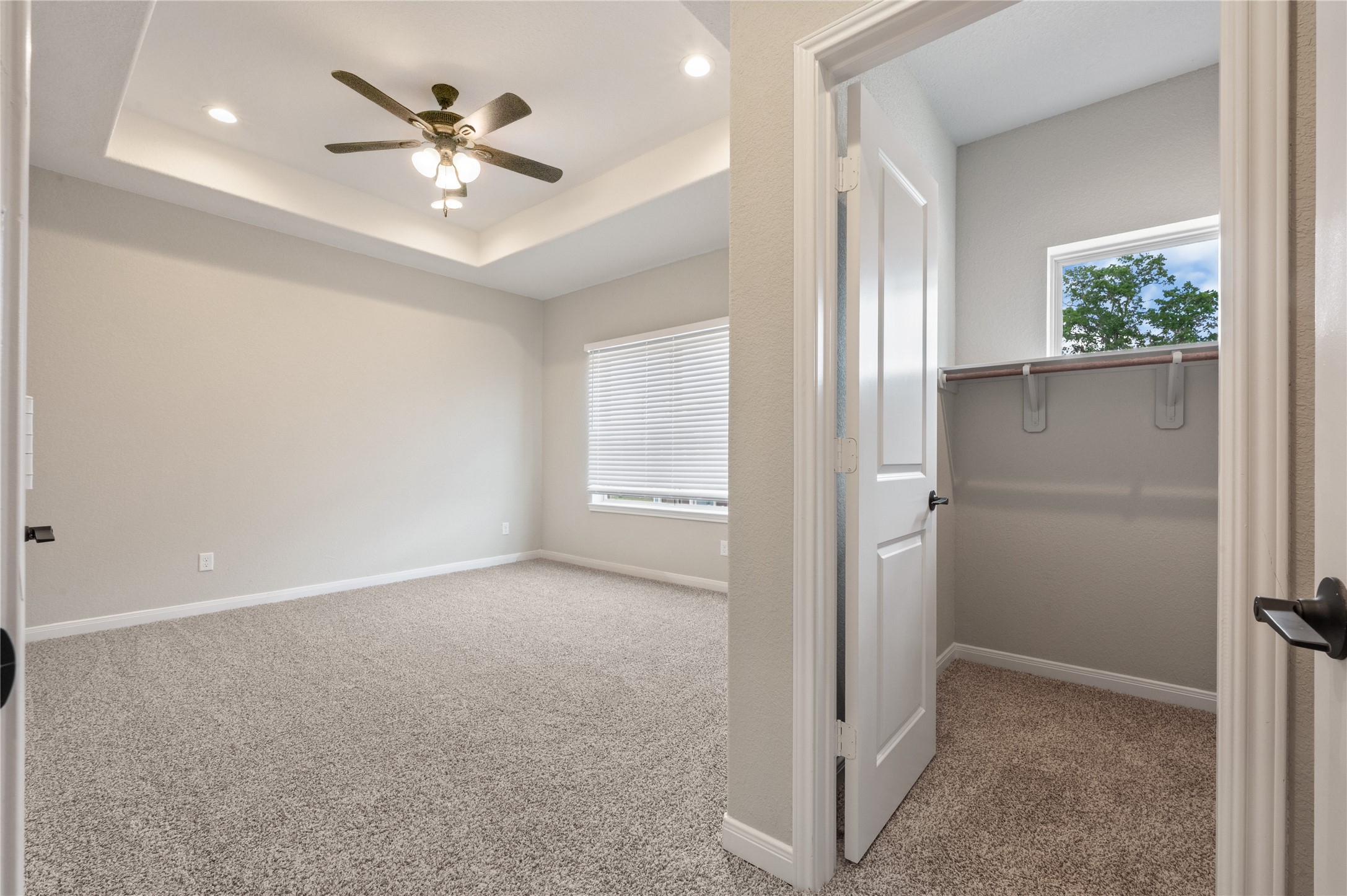 14010 Longstreet Road, Unit 2 Willis, TX 77318 - Photo 18 of 29 This photo shows a spacious bedroom with a ceiling fan and tray ceiling, featuring plush carpeting and a large window with blinds. To the right is a walk-in closet with a window, providing ample natural light and storage space.