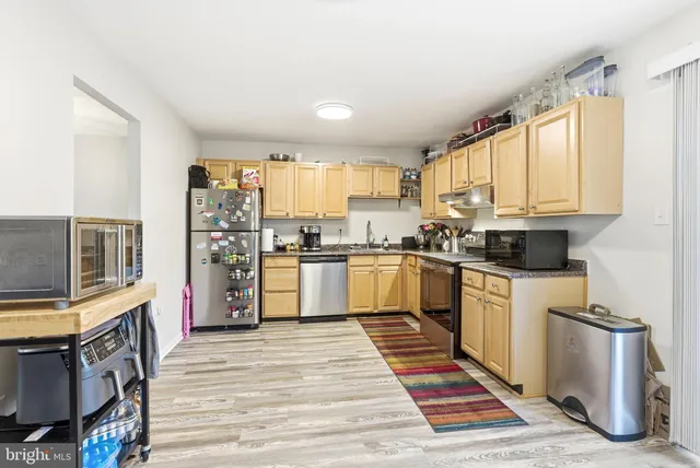 a kitchen with granite countertop a refrigerator oven a sink dishwasher and white cabinets with wooden floor